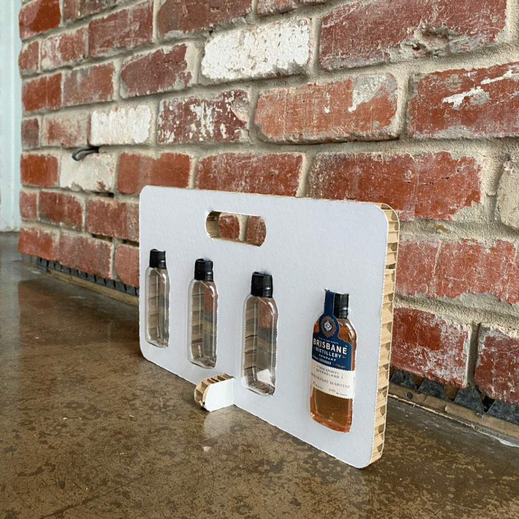 Honeycomb board insert displaying custom cut-outs securely holding glass bottles against a brick wall, demonstrating Rebul’s internal packaging design.